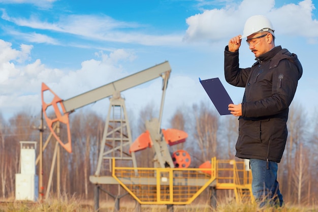 An oil geologist with a tablet next to an oil pump. Autumn