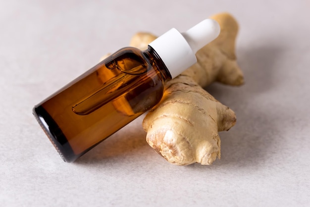 Oil of Ginger in a Small Glass Bottle Ginger Root on the Gray Background Horizontal