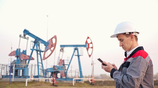 Oil industry worker with phone on the background of the oil pump, copyspace