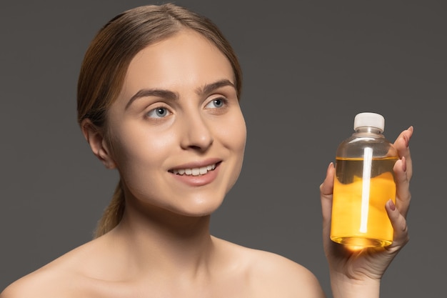 Oil. Portrait of young female fashion model isolated on grey  wall. Beautiful caucasian woman with healthy and well-kept skin. Style and beauty, skin care concept. Close up.