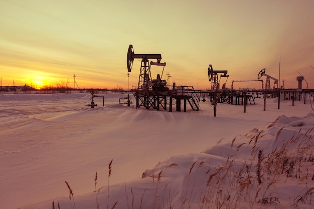 Oil pump jack on a oilfield. Winter sunset sky background. Extraction of oil. Petroleum concept. Toned.