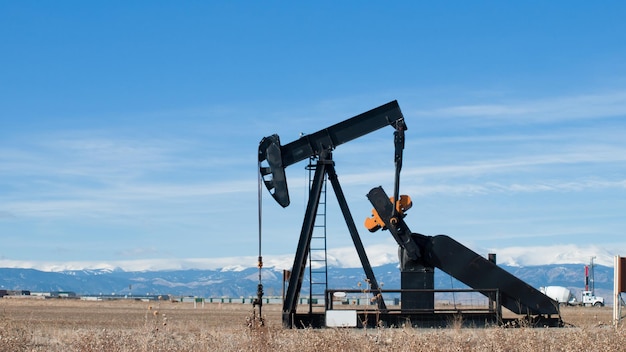 Oil pumpjack against snowy mountains in Colorado.