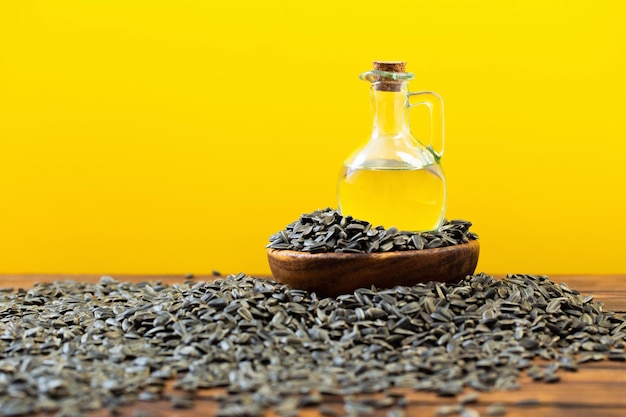 Oil and sunflower seeds on wooden table on yellow background