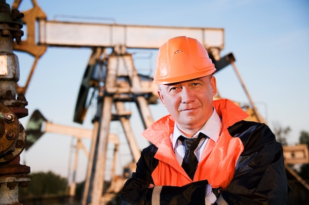 Operaio petrolifero in uniforme arancione e casco sullo sfondo della presa della pompa e del cielo blu.