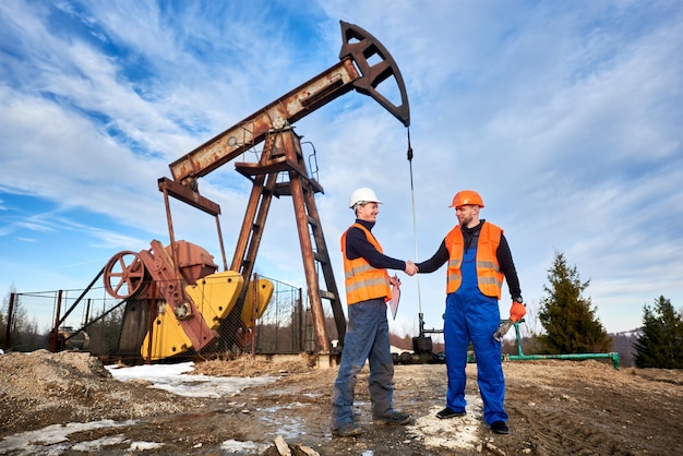 Oil workers in uniforms controlling progress work at local oil pump station on sunny day