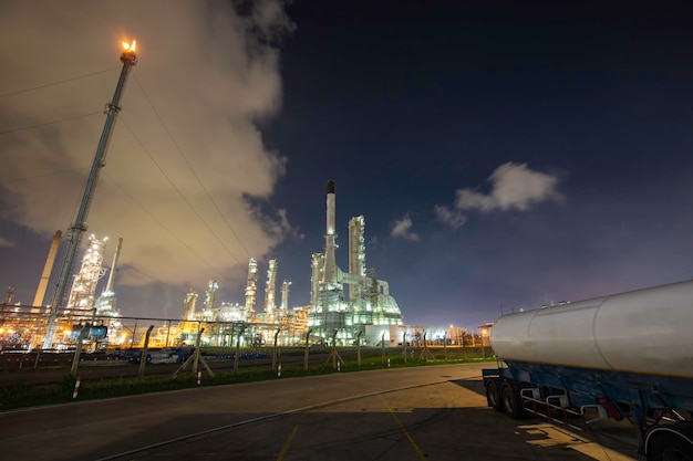 Oilâ refineryâ andâ plant and tower flare fire of\
petrochemistry in âindustry transportation truck dangerous oil\
gas truck tank is parked in the factory.