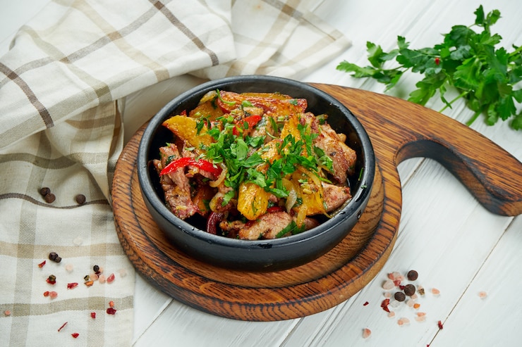 Фотография оджахури или жареное мясо с картофелем, луком и сладким перцем на черной сковороде.
