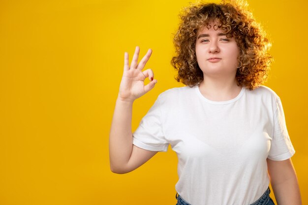 Ok gesture Body positive Overweight beauty Healthy diet Confident plus size young woman with curly hair okay hand sign isolated on copy space yellow background