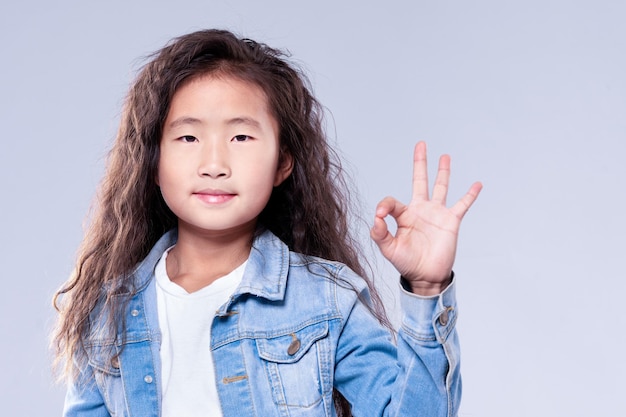 OK Girl child shows gesture fingers OK On a blue background in the studio