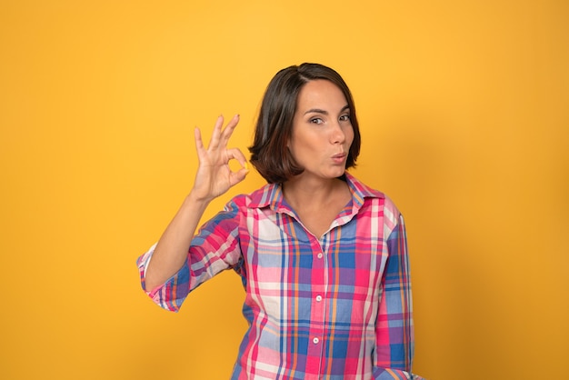 Ok or okay sign with one raised hand smile beautiful woman dressed in a plaid shirt