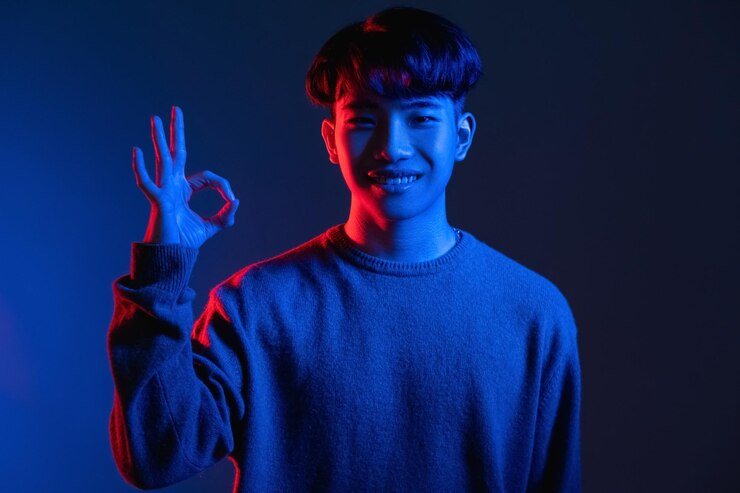 Okay gesture Approval sign Perfect choice Cyberpunk style Happy asian man guarantees best quality with OK hand symbol in red blue color neon light on dark gradient background
