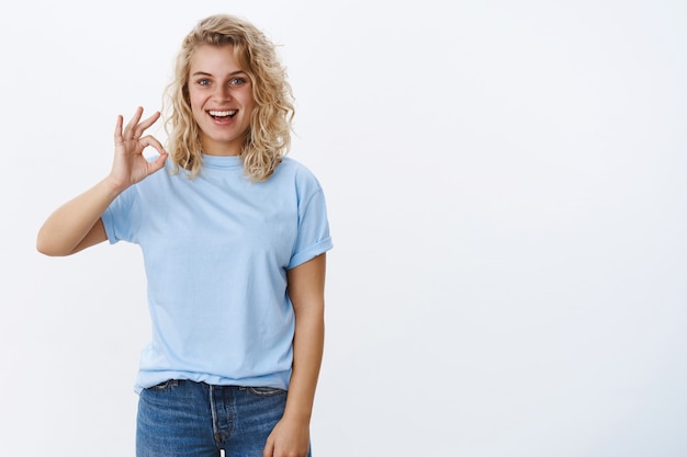 Okay I approve. Portrait of excited and pleased attractive young 25s woman with curly hair and blue eyes smiling joyfully and showing ok sign as like awesome idea, recommend product