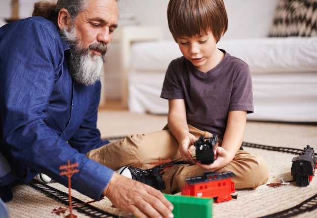 Oké opa, jij bent de conducteur en ik zal de trein besturen Bijgesneden opname van een grootvader die zijn kleinzoon ziet spelen met een speelgoedtrein