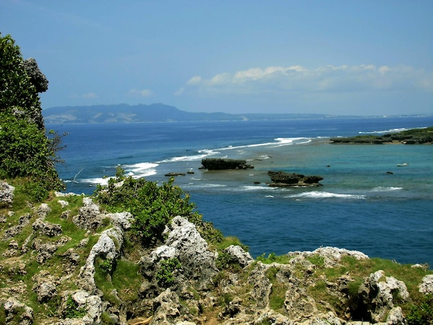 Okinawa rocky shore with a blue ocean and a mountain in the background.