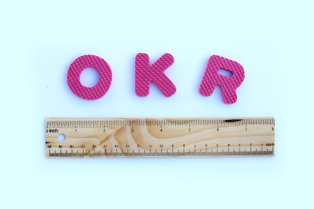 OKR alphabet with wooden ruler on white wall.