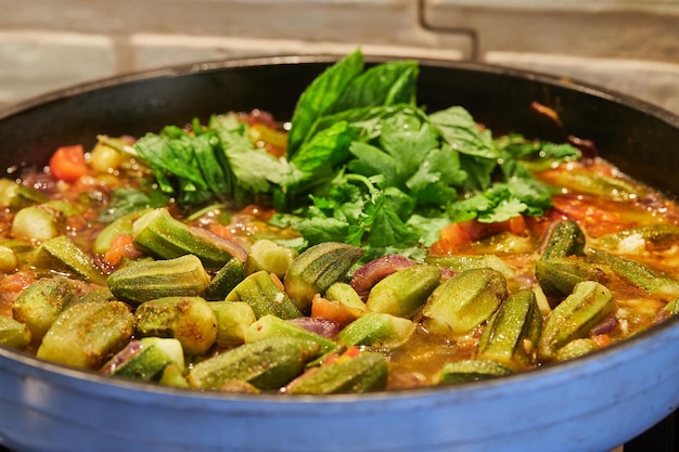 Okra and fried purple onions are panfried with cilantro and basil on gas stove