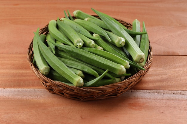 オクラまたはレディースフィンガーまたはビンディの新鮮な緑の野菜をバスケットに配置し、木製のテクスチャの背景を分離して選択的にフォーカスします