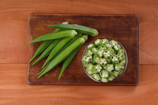 Okra or Ladys finger or Bhindi fresh green vegetable arranged  on a wooden board with a glass bowl full of okra sliced rings  with wooden background selective focus top view