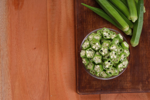 Okra or Ladys finger or Bhindi fresh green vegetable arranged  on a wooden board with a glass bowl full of okra sliced rings  with wooden background selective focus top view