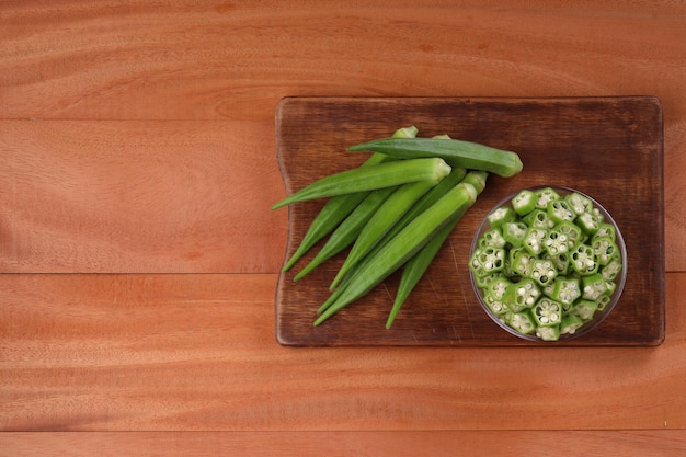 Okra of Ladys vinger of Bhindi verse groene groente gerangschikt op een houten bord met een glazen kom vol met okra gesneden ringen met houten achtergrond selectieve focus bovenaanzicht