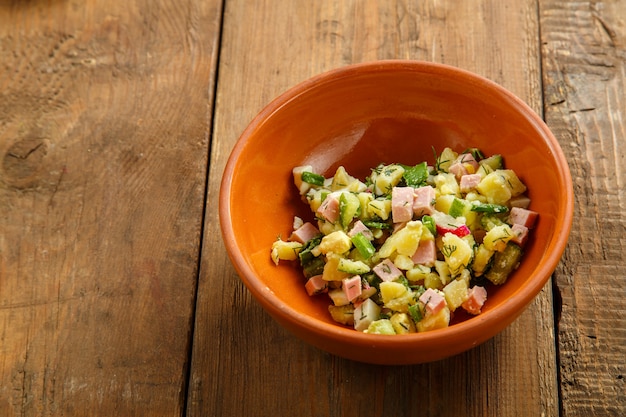 Okroshka in a clay bowl with kvass, decorated with egg and sour cream on a wooden table