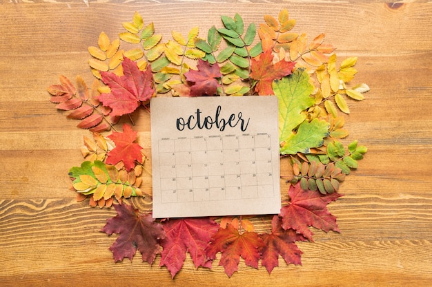 Oktober kalenderblad op houten tafel tussen rode, groene en gele herfstbladeren