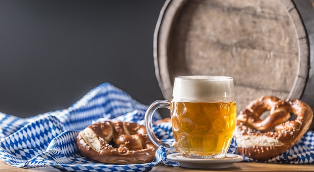 Oktoberfest beer with pretzel wooden barrel and blue tablecloth.