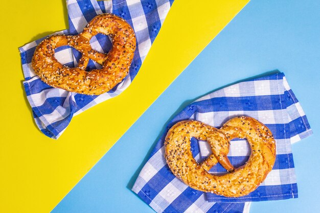 Oktoberfest concept - pretzels on a traditional napkin. Trendy hard light, dark shadow. Pastel yellow-blue background, top view