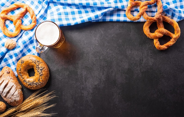 Oktoberfest festival decoration symbols made from Pretzel loaf beer sausage potato chips and Bavarian white and blue fabric on dark stone background