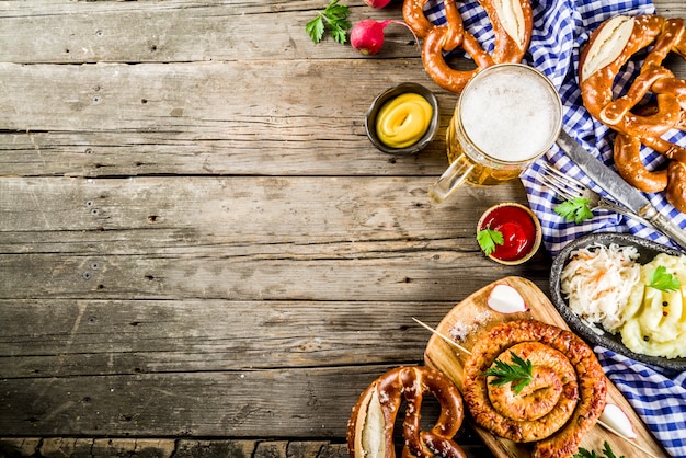 Oktoberfest food menu, bavarian sausages with pretzels, mashed potato, sauerkraut, beer bottle and mug old rustic wooden background, copy space above 