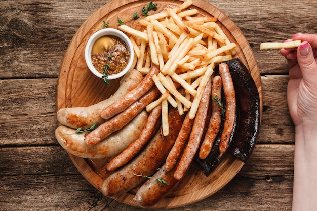 Oktoberfest maaltijd. Onherkenbaar persoon die frietjes en smakelijke gegrilde worstjes met mosterd eet, bovenaanzicht.