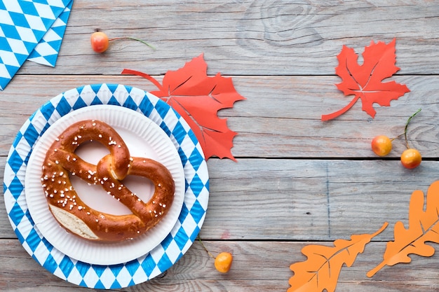 Oktoberfest rustic background with prezel in paper plate and Autumn leaves