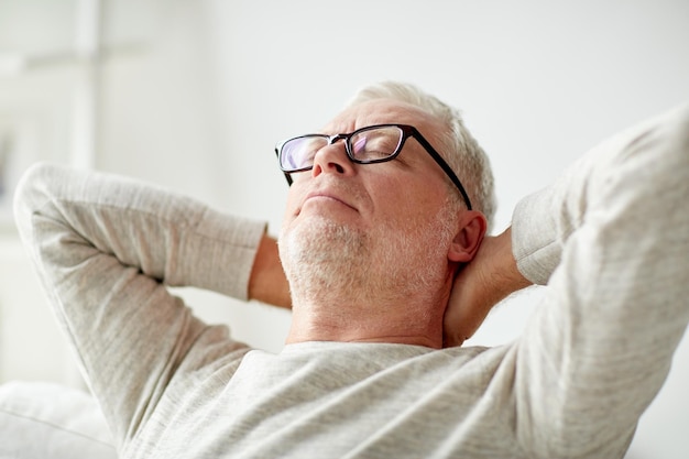 old age, comfort and people concept - senior man in glasses relaxing on sofa at home