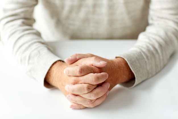 old age, gesture and people concept - close up of senior man hands on table