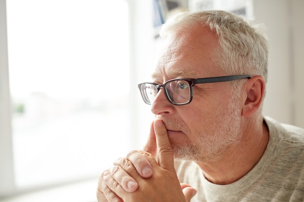 old age, problem and people concept - close up of senior man in glasses thinking