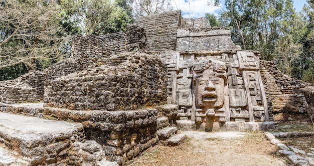 Фото Старая древняя каменная пирамида доколумбовой цивилизации майя с резным лицом и орнаментом, спрятанная в лесу археологические раскопки ламанаи район ориндж-уолк белиз