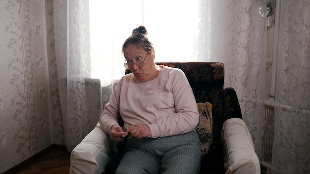 肘掛け椅子に座って編み物をしている眼鏡の老婆怒っている女性