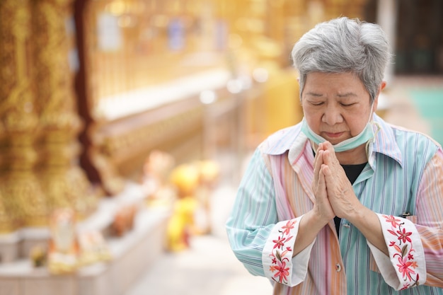 Photo old asian elder senior woman traveler tourist praying at buddhist temple.