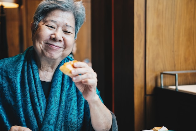 Vecchia donna anziana senior anziana asiatica che mangia pane al ristorante