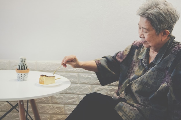 Old asian elderly senior elder woman eating cheesecake at restaurant.