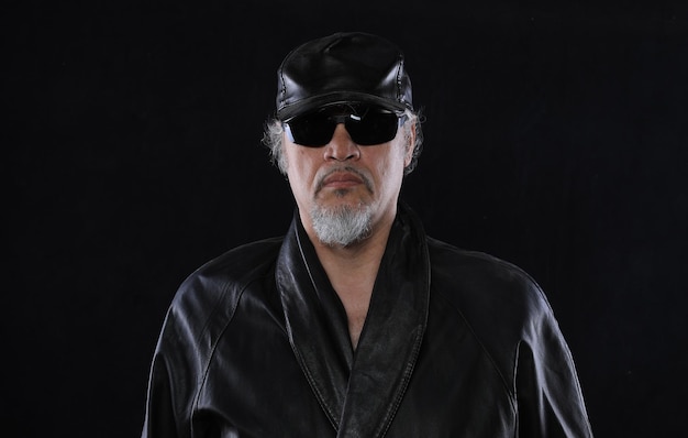 old bearded man in leather clothes on a black background