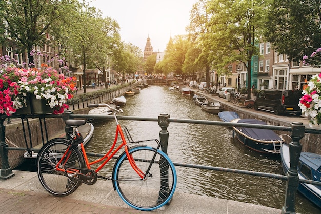 Фото Старый велосипед на мосту в амстердаме, нидерланды, на фоне канала в летний солнечный день открытка с культовым видом концепция туризма