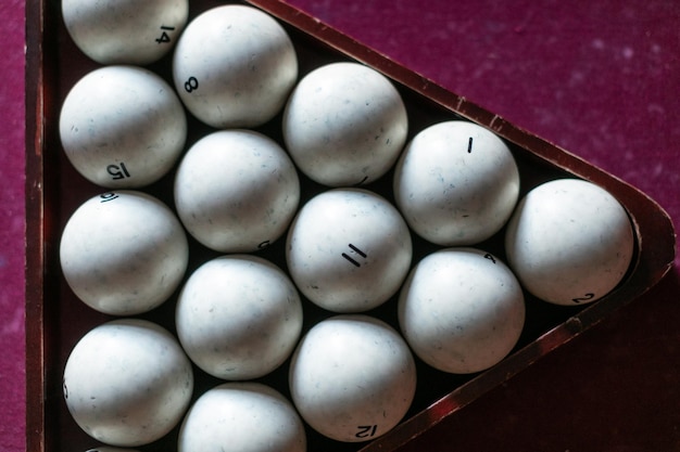 An old billiard table with red cloth and a set of white pool balls in a wooden triangular frame