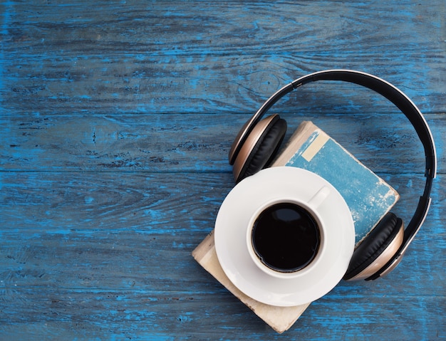 Vecchio libro, tazza di caffè e cuffie su fondo di legno scuro