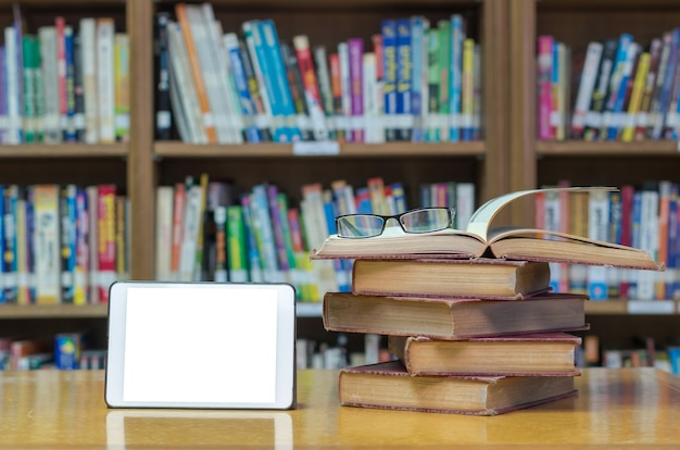 Vecchio libro sulla scrivania in biblioteca con tablet e occhiali