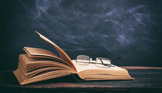 Old book and eye glasses on blackboard background