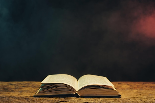 Old book on a oak wooden table Background of blue and red smoke