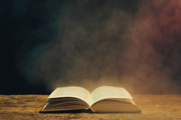 Old book on a oak wooden table Background of blue and red smoke