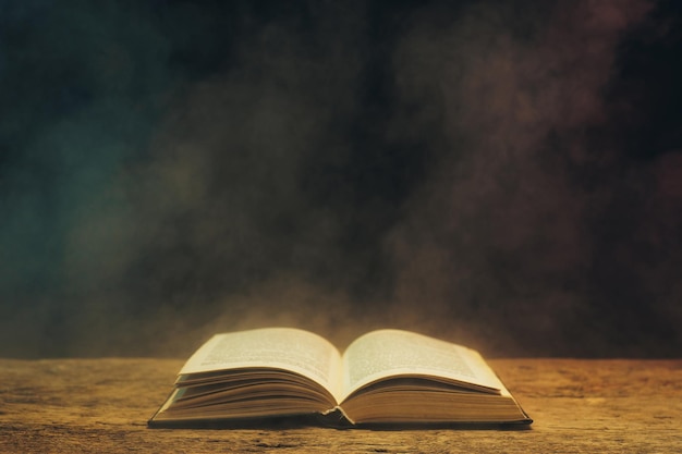 Old book on a oak wooden table Background of blue and red smoke