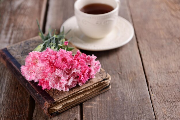 Old book with beautiful flowers and cup of tea on wooden table close up